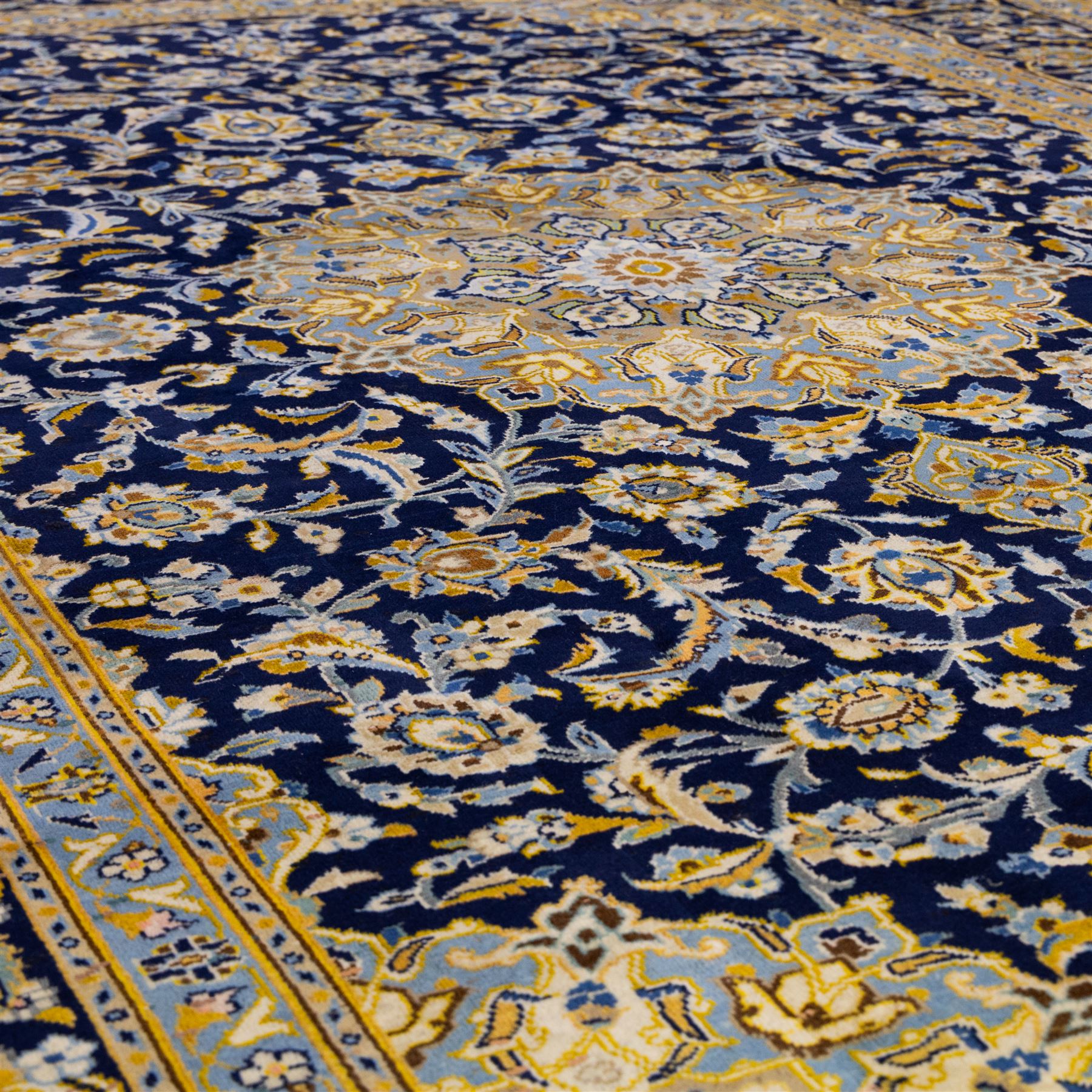 Central Persian Kashan hand-knotted rug, deep indigo field with central floral medallion surrounded by an all-over arrangement of palmettes, flowering vines, and tendrils with matching spandrels enclosed by a pale blue floral main border with multiple narrow guard stripes, with cotton fringe ends 