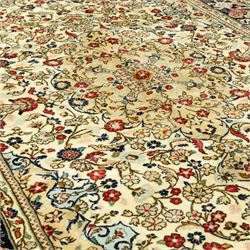Central Persian Kashan hand-knotted carpet, ivory ground, with an all-over floral field centred by a subtle shaped medallion, surrounded by scrolling foliate and floral motifs incorporating rosettes, palmettes and delicate vine work, enclosed by a dark navy border with repeating palmettes and meandering vines, flanked by floral guard stripes, with cotton fringes