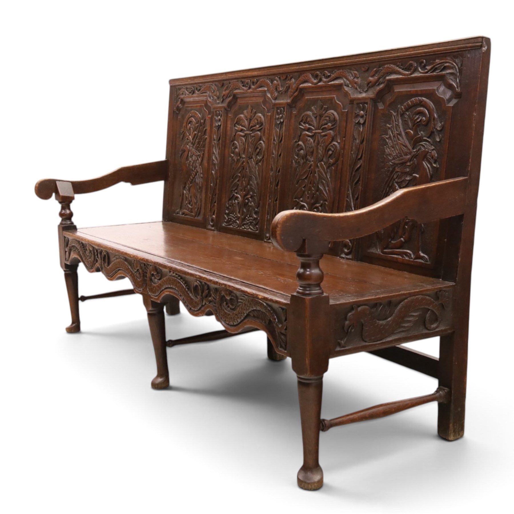 19th century Gothic Revival heavily carved oak settle or hall bench, the high quadruple back with moulded cresting rail over a frieze carved with stylised dolphin and sea creature motifs, the panels decorated with griffin and bird motifs with floral dividing rails, the shaped apron similarly carved with scaly sea beasts, on three cabriole front-supports united by stretchers
