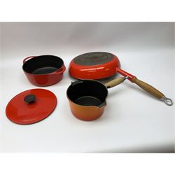 Le Creuset 'Volcanic Orange' cast iron and enamel milk pan with wood handle together with a three piece red cast iron Cousances saucepan set of graduating form, with lids housed in original wooden hanging stand and further Cousances lidded casserole dish and pan