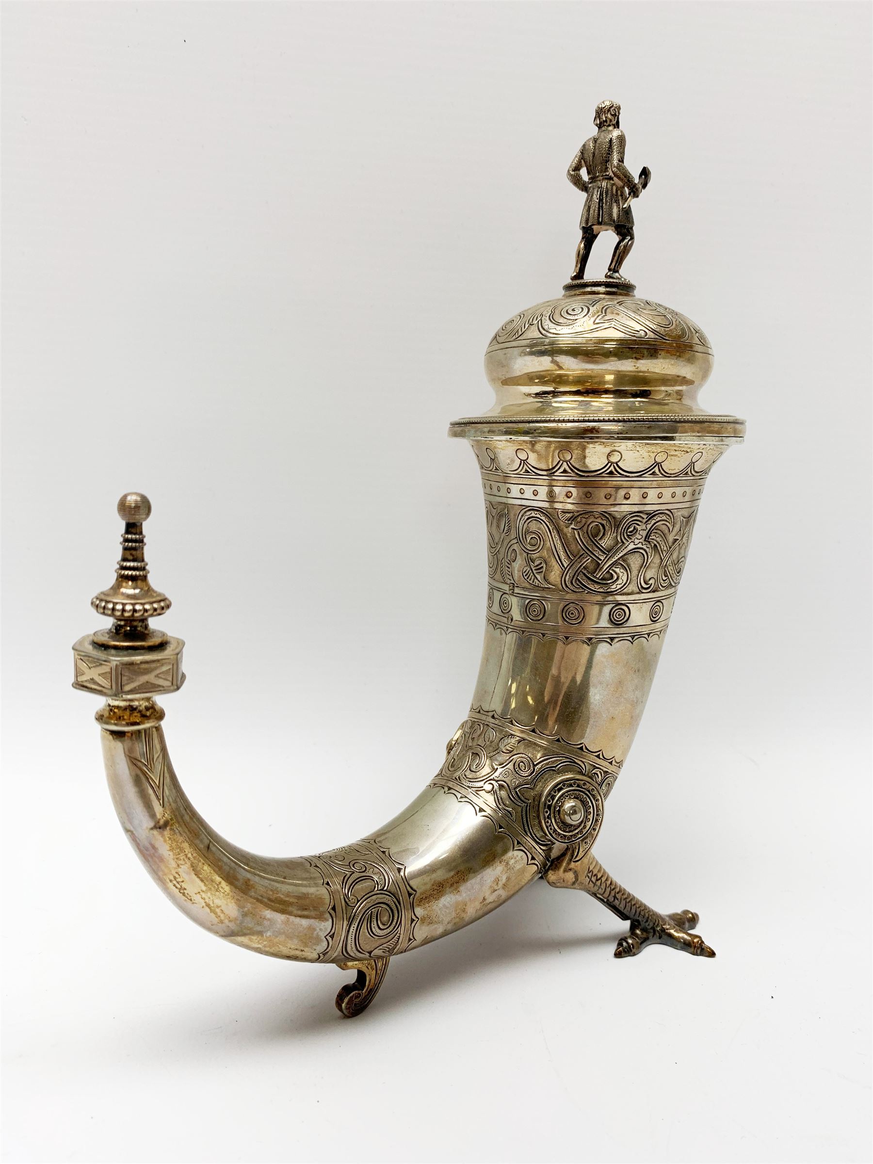 Late 19th century Danish silver drinking horn and cover, the body with hexagonal and beaded finial, raised upon two talon feet and further scroll foot, chased with scrolling foliate and zoomorphic bands, the detachable domed cover with conforming decoration surmounted by a figure holding a hammer, the cover interior impressed with maker's mark (partly worn and indistinct), alongside Danish Three Towers mark for 1881, with the Assay Master mark for Simon Groth (1863-1904), H23.5cm, weight 14.75 ozt (459 grams)

