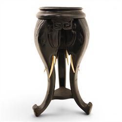 Oriental design black lacquered jardinière stand, circular moulded top with raised rim, the base formed as three elephant heads with carved ears and simulated tusks, on shaped supports with paw terminals
