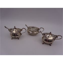 Three silver mustard pots with covers, comprising pair with acanthus capped handle, engraved initial to body and upon four paw feet, hallmarked Horton & Allday, Birmingham 1899, and an oval example with par fluted decoration throughout, hallmarks worn and indistinct, all with blue glass liners and matched hallmarked silver spoons