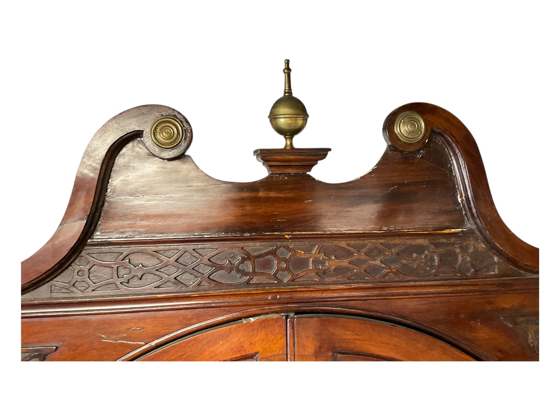 George III mahogany corner cabinet, the scrolled pediment surmounted by a brass finial and carved fretwork frieze, with fluted uprights flanking arched double doors over a painted interior fitted with shaped shelves, above a lower cupboard with twin panelled doors, on plinth base