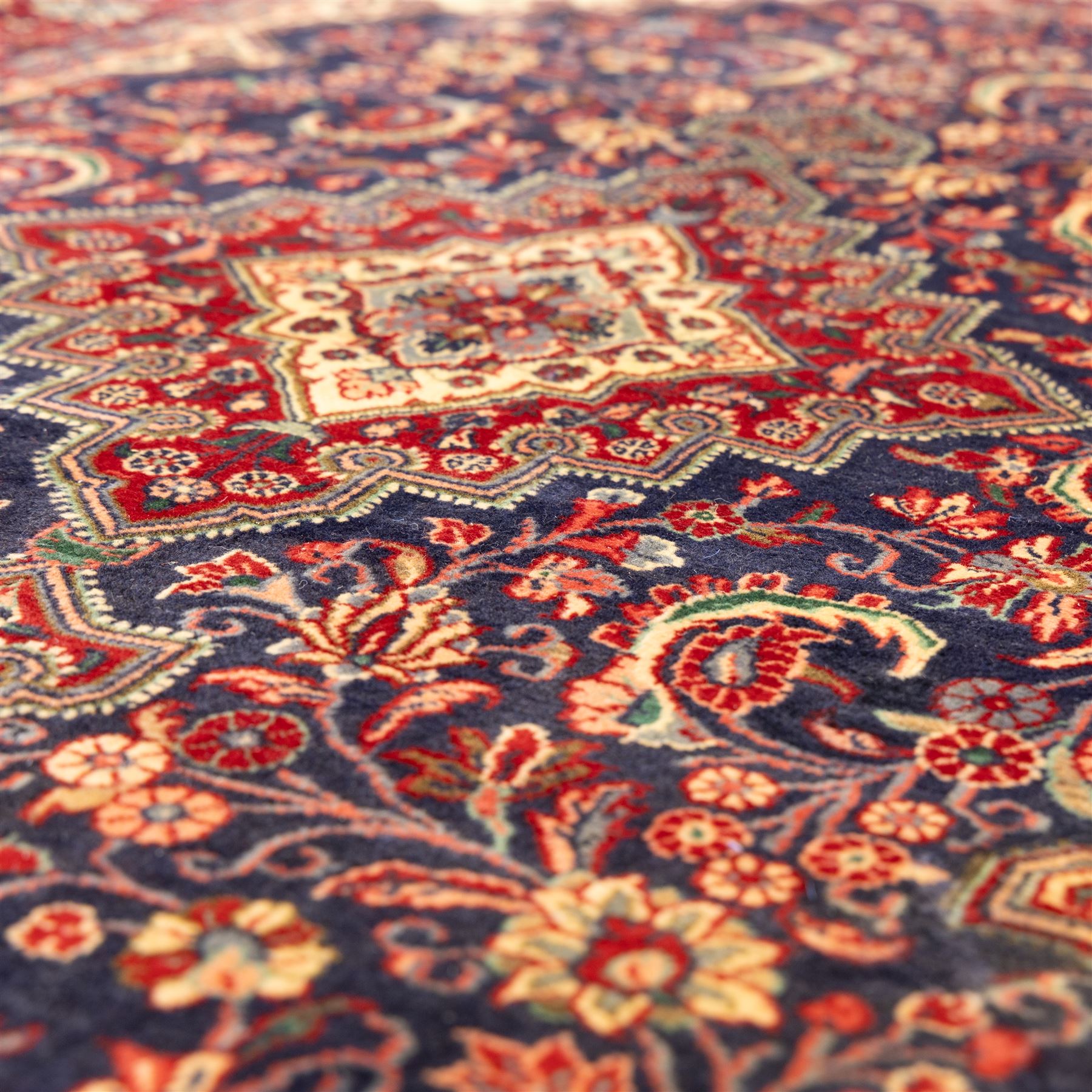 North West Persian hand-knotted Sarouk rug, central navy ground field with cusped lozenge medallion with pendant motifs, scrolling palmettes, and floral sprays, cream spandrels, and madder red border of stylized rosettes and leafy meandering vines between multiple guard stripes 