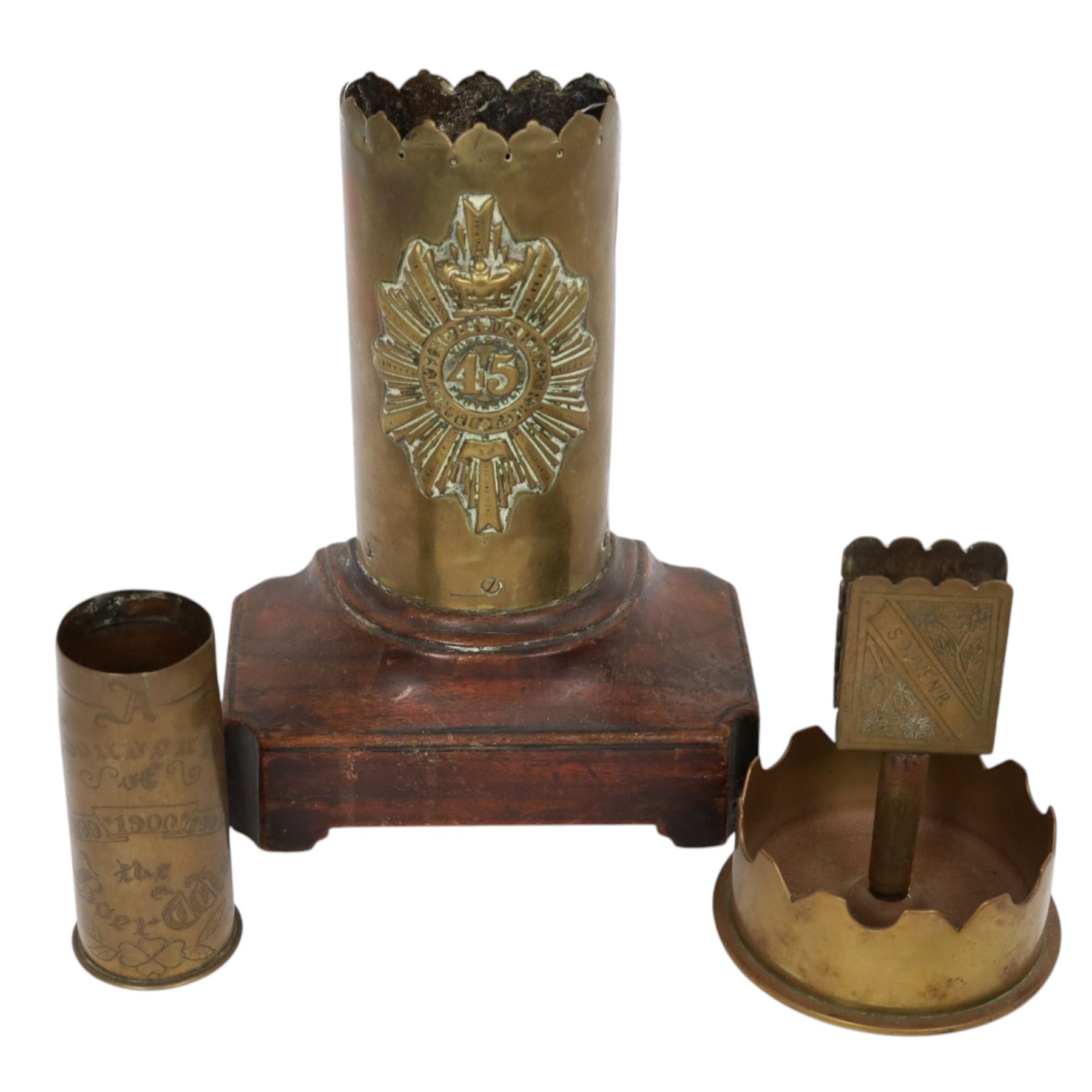 Collection of trench art, including a vase with scalloped rim, applied with a helmet plate to the 45th regiment, mounted on a canted rectangular walnut plinth, together with ashtray with matchbox holder to the center, pair of Boer war vases etc 