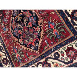 Persian Hamadan rug, the red ground field decorated with two floral medallions and stylised flower heads, repeating guarded border