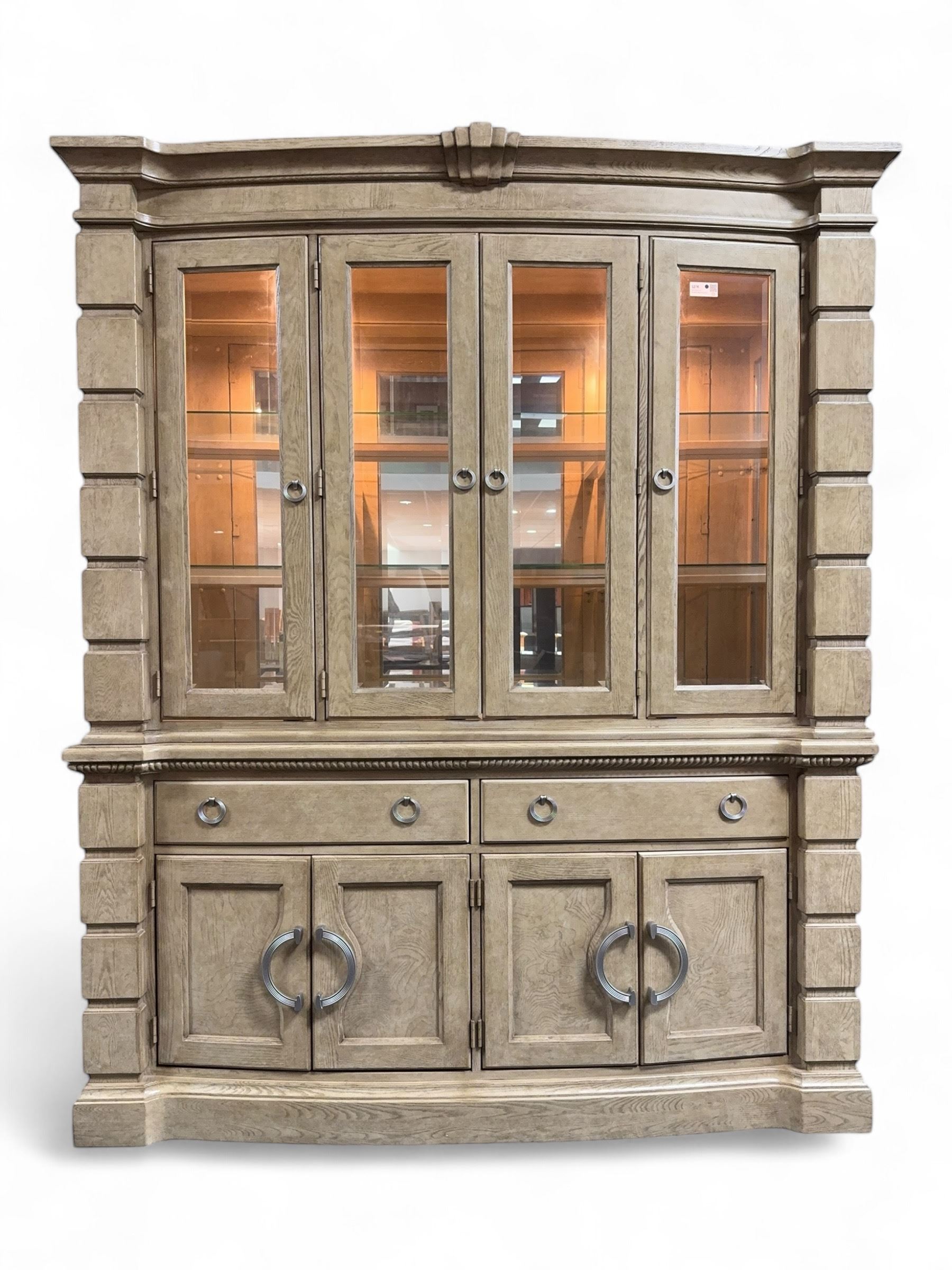 Brunswick - washed oak finish illuminated display cabinet, upper section with four glass-panelled doors enclosing glass shelving, base fitted with two drawers over four paneled cupboard doors, each fitted with distinctive round metal handles, raised on plinth base