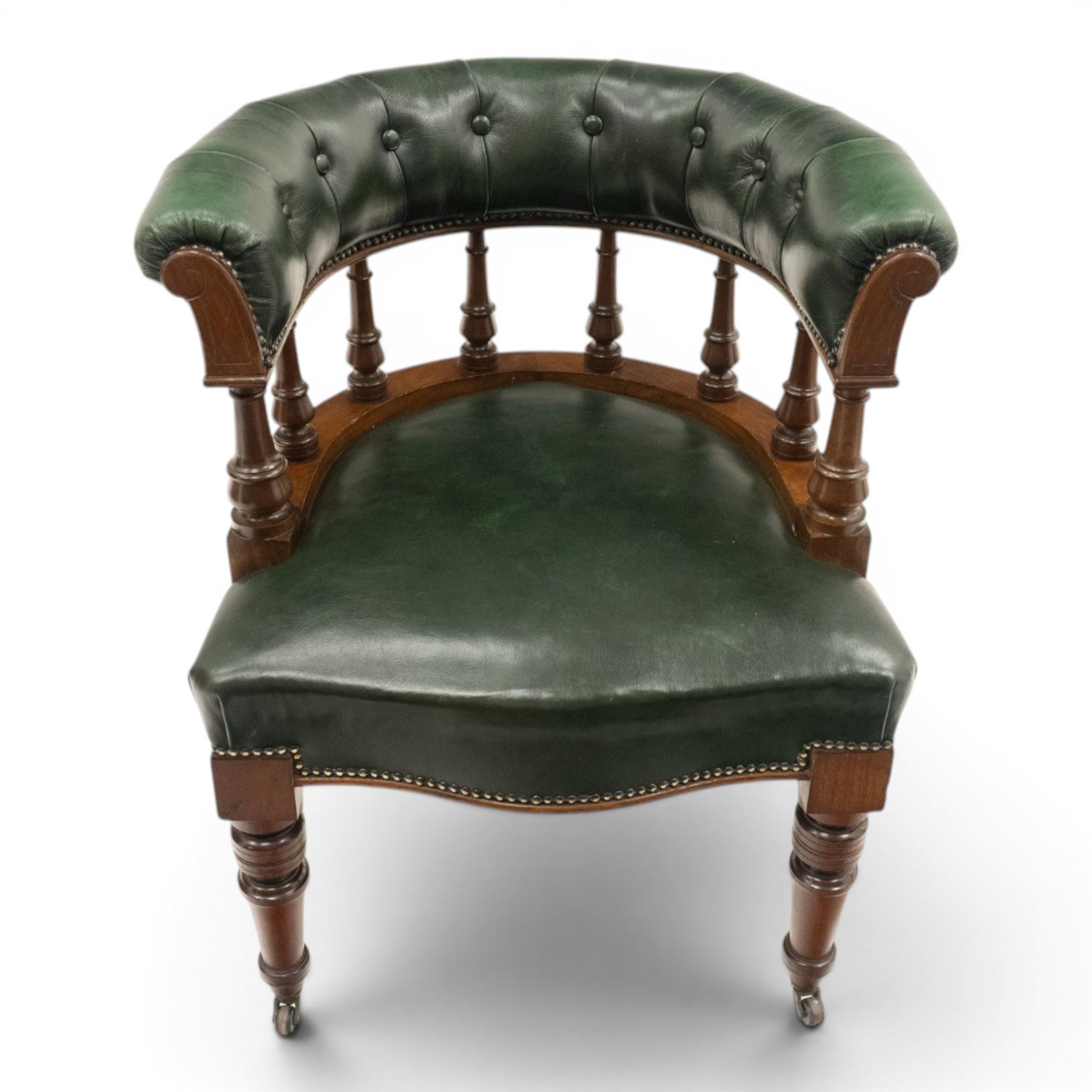 Late Victorian mahogany framed Captains tub desk chair, the green leather upholstered cresting rail over turned spindle supports over a sprung seat, raised on front turned supports terminating to ceramic castors