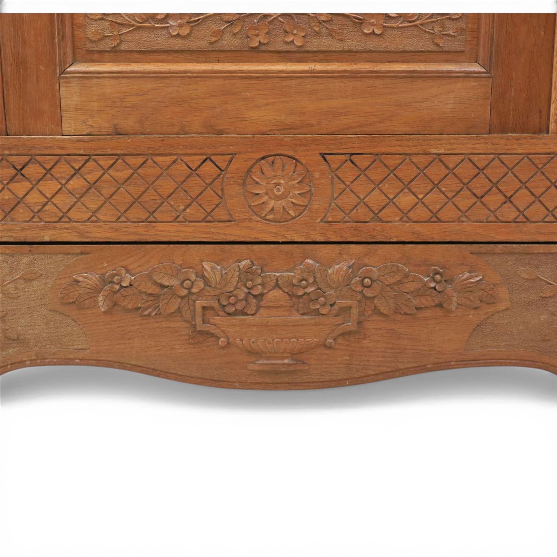 Early 20th century French oak triple door armoire, the moulded top above a frieze with carved lozenge decoration and central rosette, the central mirrored door enclosed by carved surround with floral crest, flanked by panelled doors with lattice carving, the base with shaped apron centred by carved basket motif, upon shaped cabriole supports