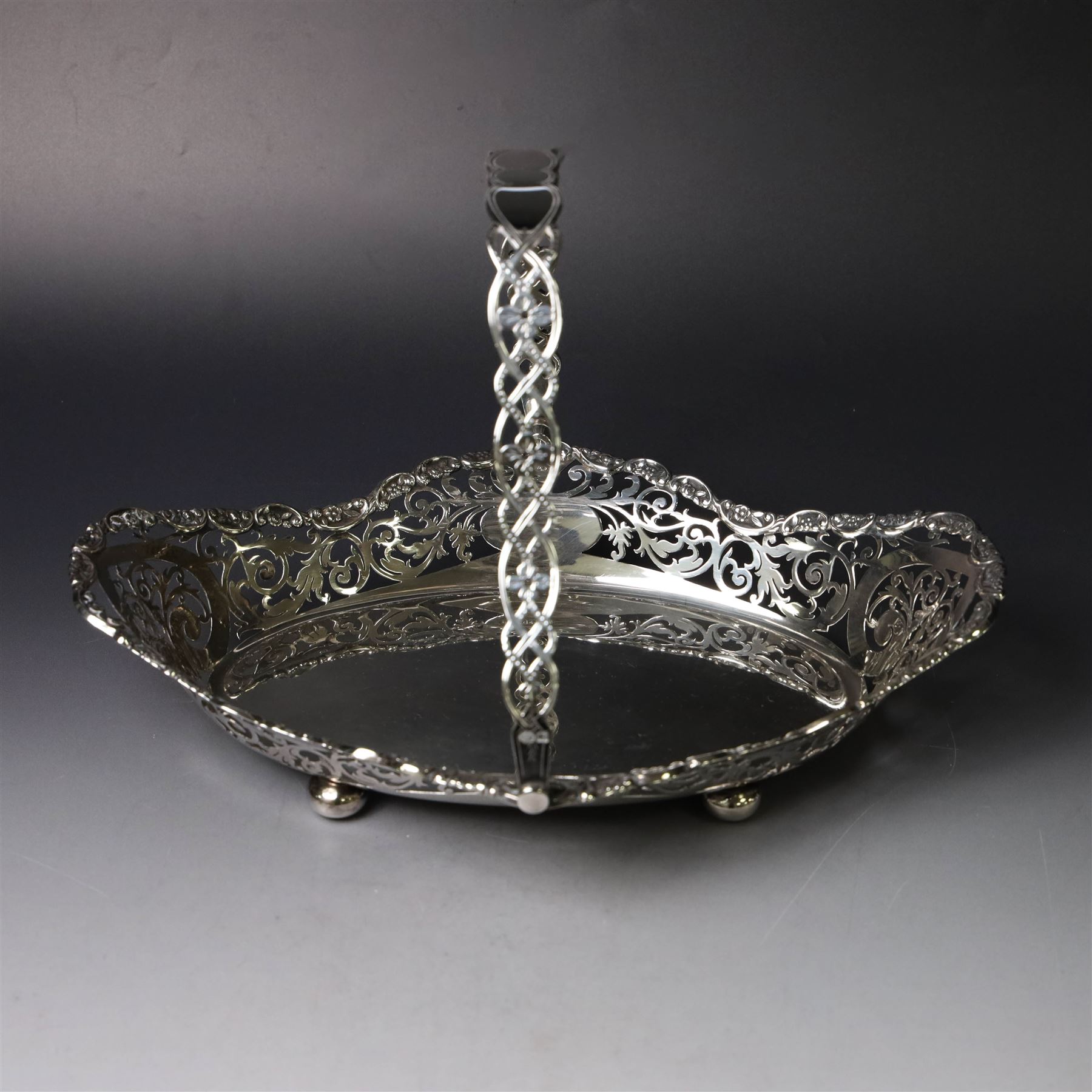 Early 20th century swing handled basket, of oval form with pierced sides and floral C scroll rim, upon four bun feet, hallmarked William Hutton & Sons Ltd, Sheffield 1915, widest point W29cm