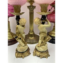 Victorian cast brass oil lamp, with fluted pink glass shade, together with two smaller brass oil lamps with pink shades and reservoirs and a pair of oil lamps, the bases modelled as putti, with pink glass reservoir  and frosted shades, tallest H70cm