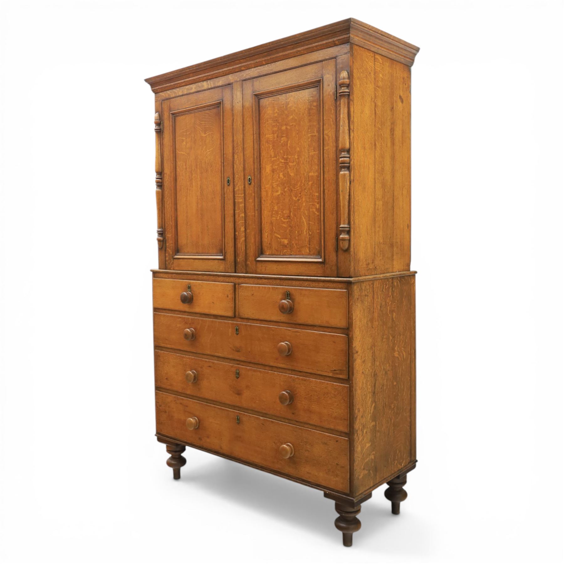 Late 19th century country oak cupboard on chest, cornice top above twin recessed panel doors with central escutcheons, flanked by turned pilasters, the lower chest with two short and three long drawers fitted with turned knob handles, on turned feet