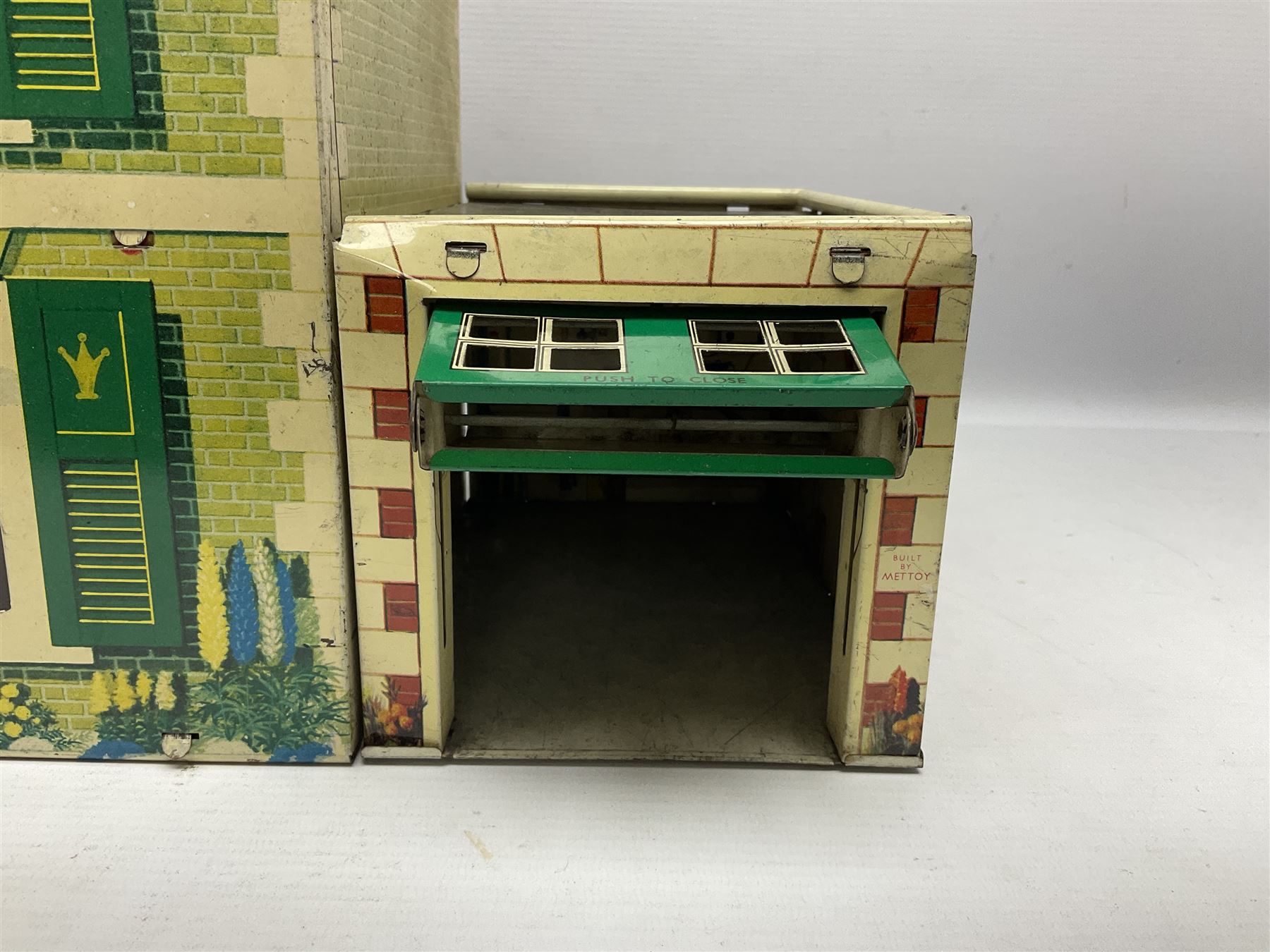Mid-20th century Mettoy tin-plate double-fronted two-storey doll's house, the front elevation with five unglazed windows flanked by green shutters, central opening door, open back giving access to five rooms together with an attached garage, 60cm wide