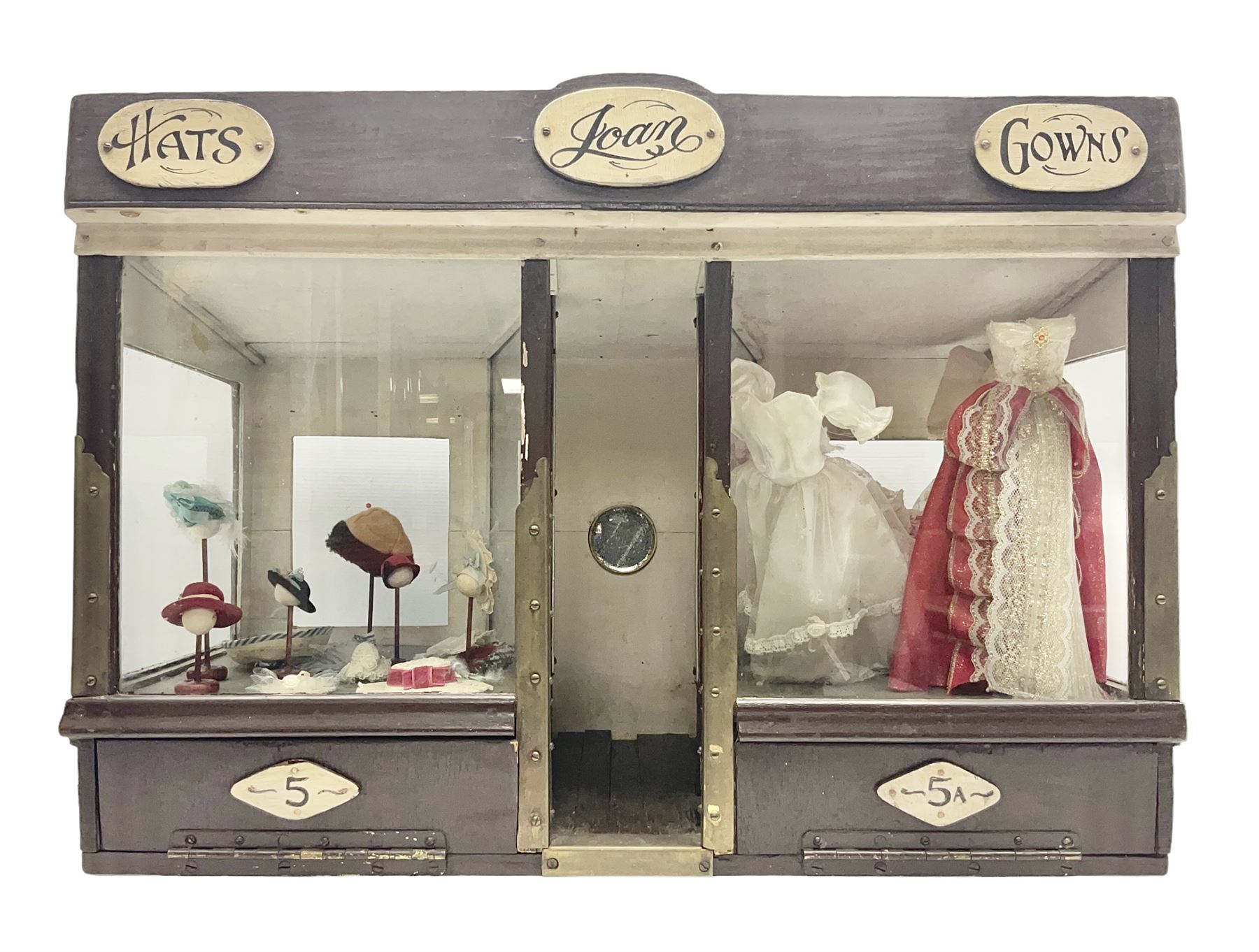 Early 20th century scratch-built wooden hat & gown shop diorama 'Joan', of double-fronted form glazed on three sides with brass and aluminium mounts, rear access apertures and storage under L63cm H45cm D31cm; with small collection of dresses and hats on display stands