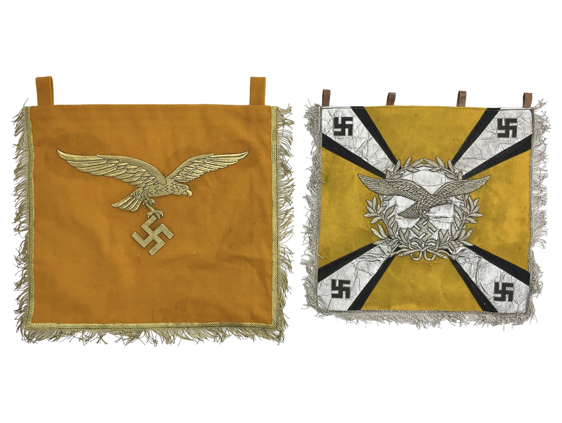 Two replica German Luftwaffe trumpet banners, one heavily silver wire embroidered with Luftwaffe eagle in a wreath, on an amber, white and black rayed background, , with silver wire tasselled border and four leather hanging loops, approx. 50 x 49cm; the other slightly larger heavily gold wire embroidered with the Luftwaffe eagle on a plain amber ground with gold wire tasselled border and two hanging loops (2)