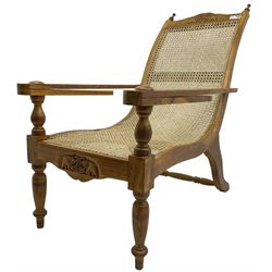 Late 20th century teak framed plantation chair, cresting rail and apron carved with two elephants with upraised trunks, flanked by finials, cane back and seat, fitted with hinged extending leg rests, on ring turned supports