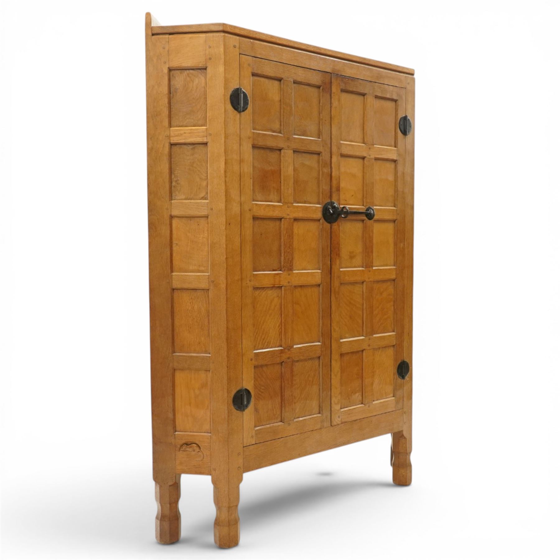 Mouseman - 1940's adzed and panelled oak corner cupboard, the raised quarter-gallery back over twin adzed panelled doors with wrought iron fittings and latch, enclosing three shaped shelves, raised on turned octagonal supports, with carved mouse signature in relief, by the workshop of Robert Thompson of Kilburn Provenance: purchased directly from the Kilburn workshop in the late 1940s