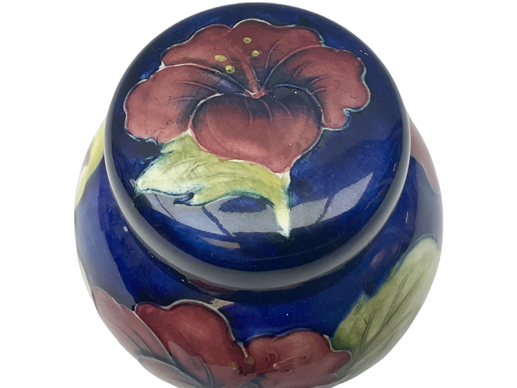Moorcroft ginger jar, decorated in the Hibiscus pattern upon a blue ground, with paper label beneath detailed 'Potters to the late Queen Mary', H11cm.
