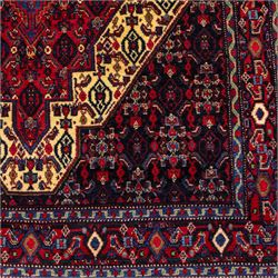 North West Persian Senneh hand-knotted rug, dark indigo field with a central bold stepped lozenge medallion of madder red and deep blue, enclosed within an ivory serrated contour forming a cruciform outline, medallion with repeating boteh and floral devices, field decorated with an all-over Herati pattern of rosettes enclosed by angular leaves principal border of madder red ground decorated with alternating floral heads, flanked by narrow guard stripes, with cotton fringe ends 