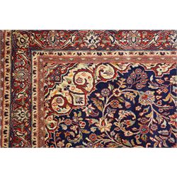 Central Persian Kashan hand-knotted rug, indigo field with central lobed medallion with pendants issuing scrolling arabesque of palmettes, flowering vines, and foliate tendrils, with conforming spandrels, with vine border and framed by guard stripes in tones indigo, ivory and madder red, with cotton fringe ends 