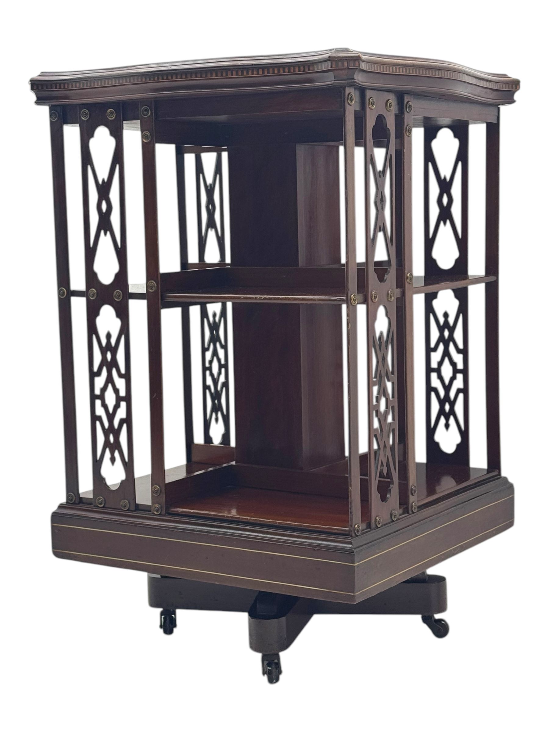 Edwardian inlaid mahogany revolving bookcase, shaped square moulded top with central motif and satinwood band, two tiers with pierced vertical splats, on swivel action base with ceramic castors
