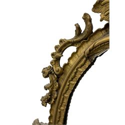 19th century gilt wood and gesso wall mirror, the cartouche pediment over oval shell scalloped frame with foliate moulded inner slip, the frame mounted by trailing and scrolled leafage with C-scrolls, the lower shaped section decorated with foliage and fruit, plain mirror plate 