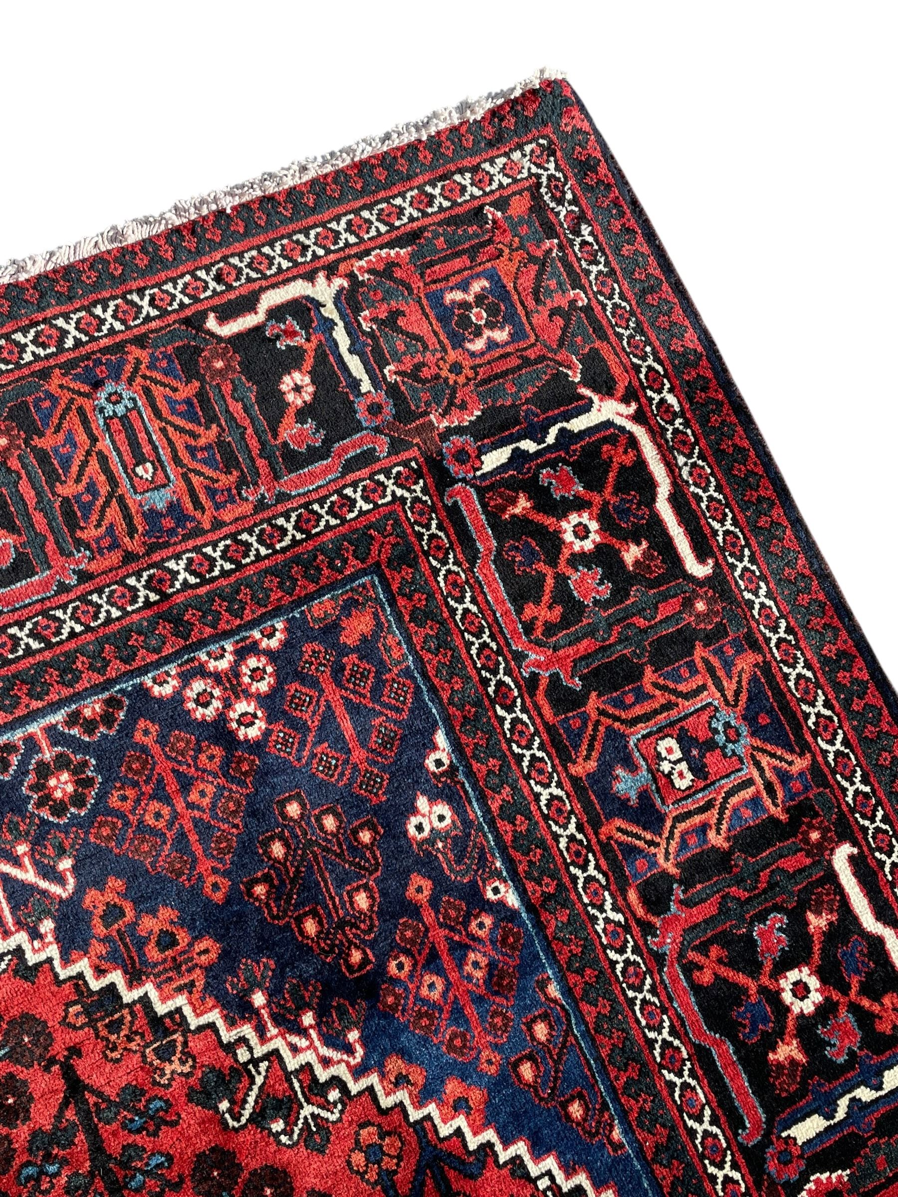 Persian Joshaghan crimson ground rug, stepped lozenge medallion surrounded by repeating foliate lozenge motifs, the border decorated with stylised plant motifs, within geometric guard stripes