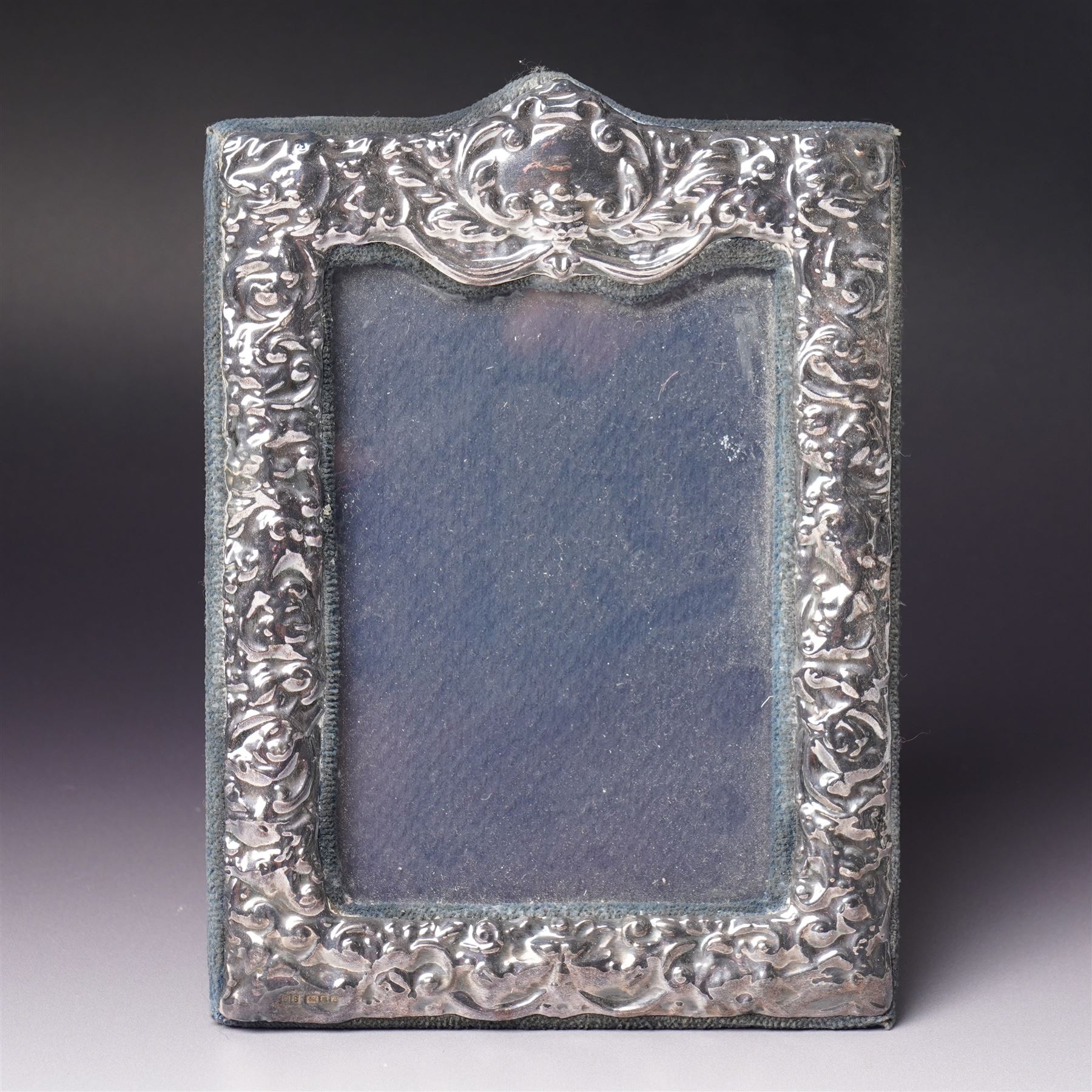Embossed silver photograph frame London 1985 aperture 12.5cm x 8.5cm, another with scroll top Birmingham 1921 13cm x 9cm and a circular frame Birmingham 1909 6cm