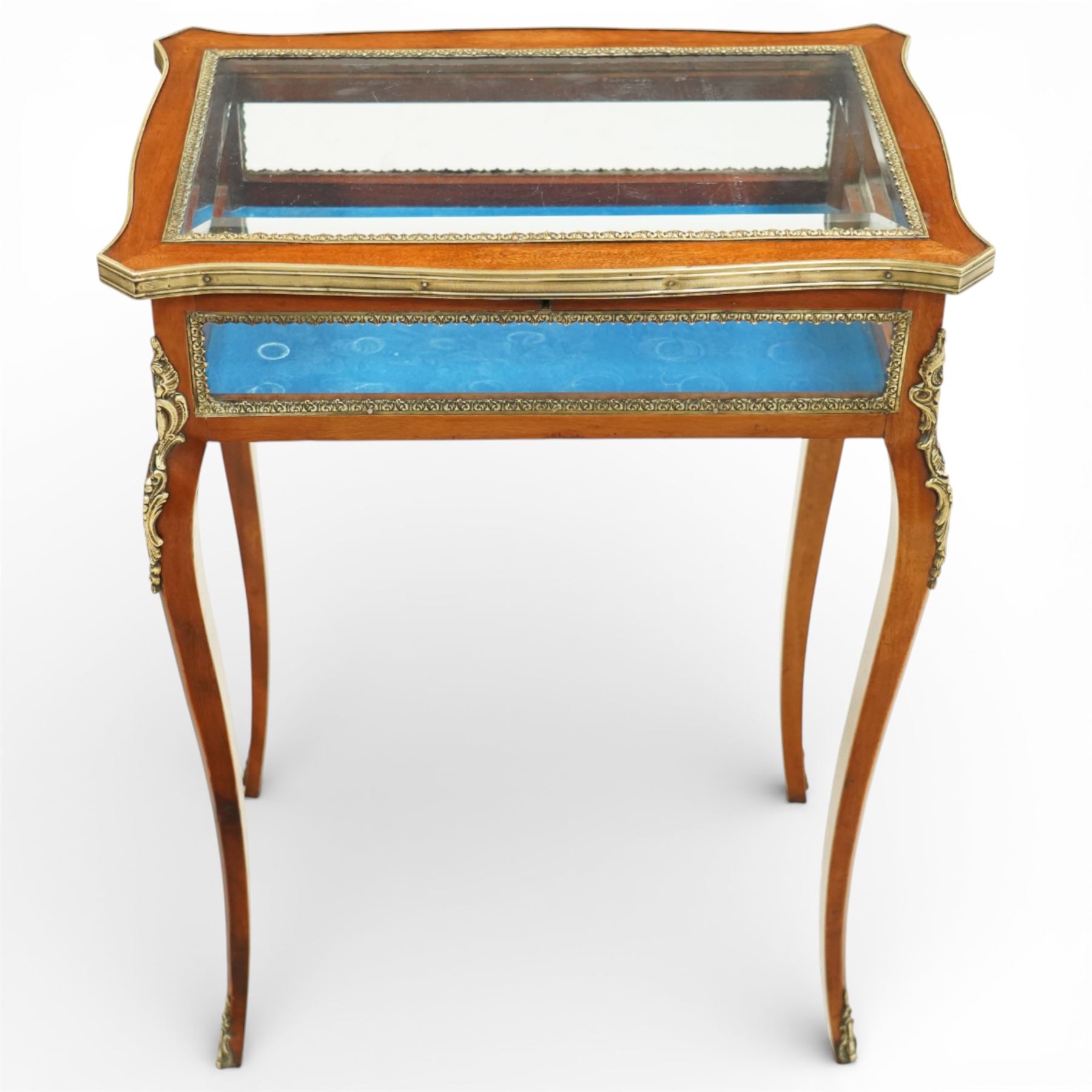 Early 20th century French mahogany bijouterie table, the hinged shaped rectangular top with brass edge and gilt-metal foliate slip enclosing bevelled glass plate, raised on cabriole supports with applied gilt-metal cartouche and foliate mounts