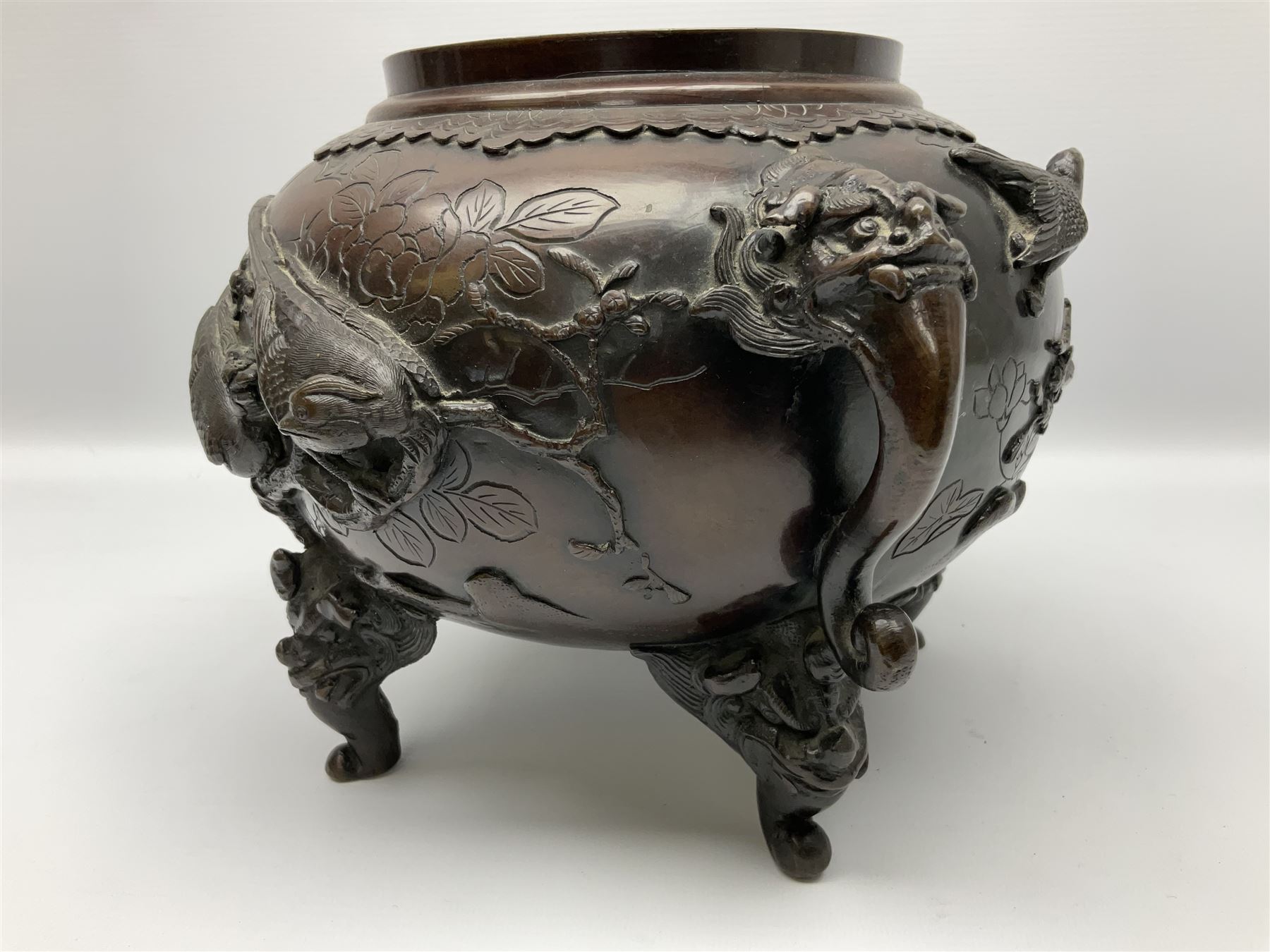 Japanese bronzed koro, the body of globular form with twin cast zoomorphic mask handles, decorated in relief with birds upon blossoming branches, against a ground incised with rushes and peonies, the flat toped domed cover with pierced band and surmounted by a cast figure of a Foo dog, the whole upon three zoomorphic mask feet, with impressed character type mark beneath, H35.5cm