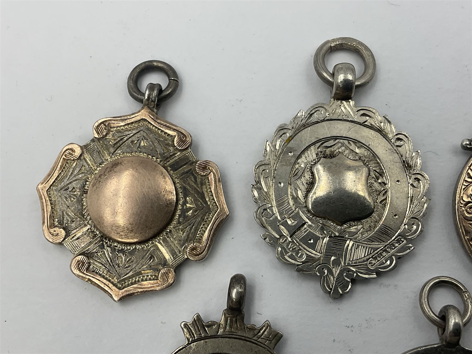 Seven early 20th century silver gold faced cartouche fobs, to include a circular example, with rose gold border and cartouche within an embossed yellow gold border, engraved verso, and a double sided example, all hallmarked with various dates and makers
