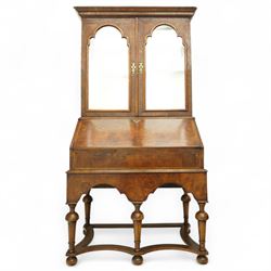 Queen Anne burr walnut chest on stand, moulded projecting cornice over arched mirror glazed doors, above a sloping fall front enclosing fitted interior with pigeonholes and correspondence drawers, fitted with foliate brass escutcheons, shaped apron over tapered baluster turned supports united by curved stretchers, early 18th century with later restorations 