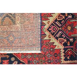 Persian Hamadan crimson ground rug, the indigo field decorated with a central geometric medallion, filled and surrounded by stylised plant motifs, the guard bands with further geometric decoration