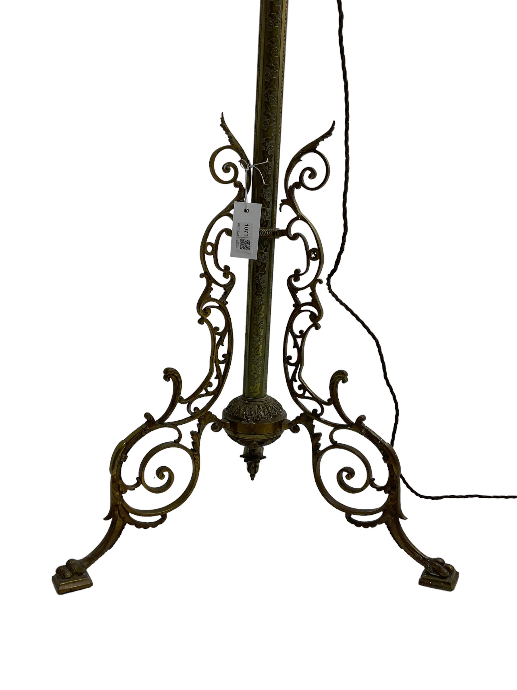 Victorian brass floor standing oil lamp, column decorated with ivy and acanthus leaves, the tripod base pierced with scrolled foliate decoration, with ivory and gilt shade, later converted to electricity