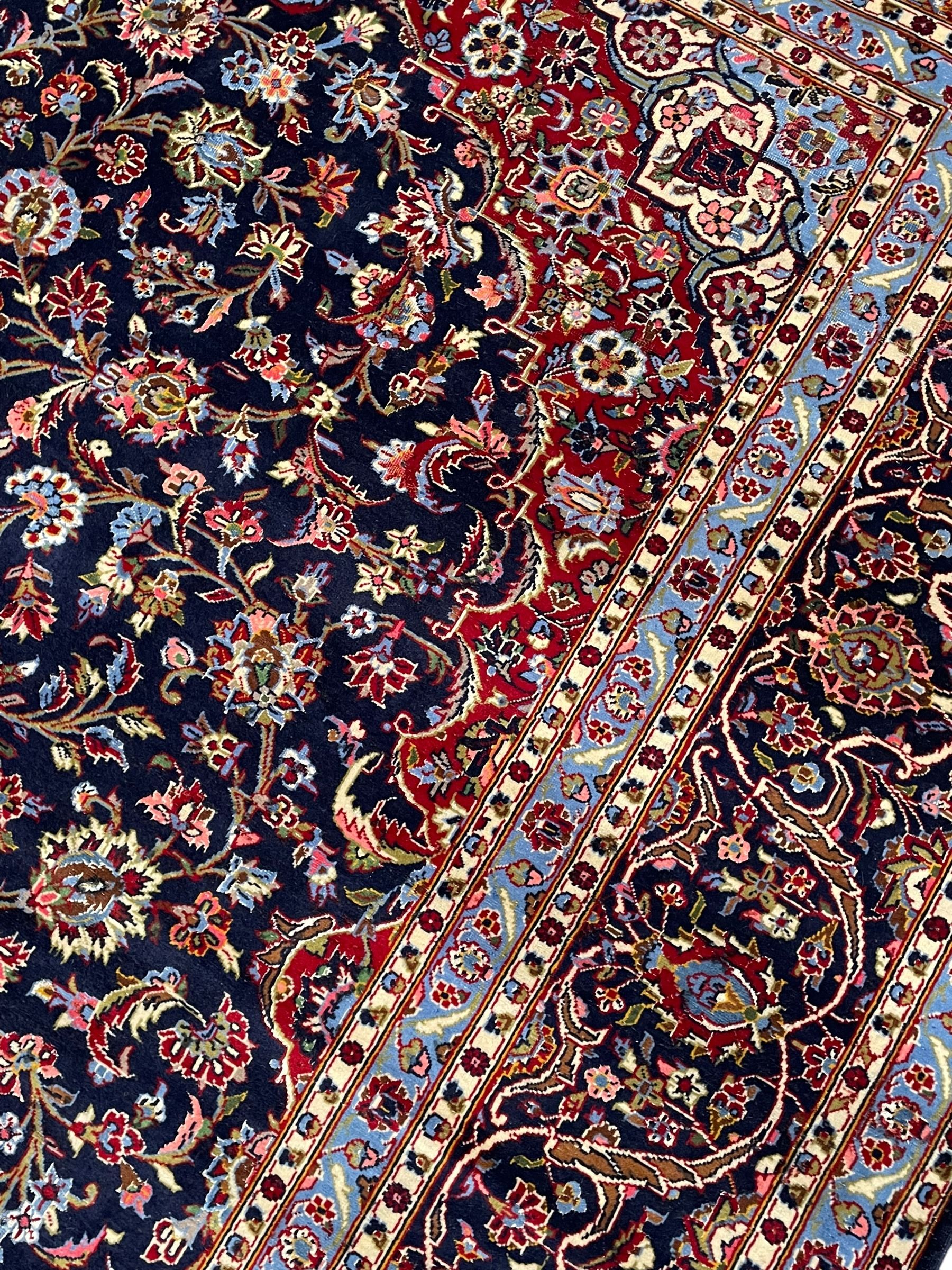 Persian Kashan indigo ground carpet, central floral pattern medallion surrounded by a densely decorated field depicting trailing branches with leaves and palmettes, scrolling border decorated with stylised plant motifs, within floral pattern guard stripes 