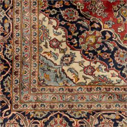 Persian Kashan carpet, the field in rich rust tone centred by an ivory and blue medallion with palmette extensions, surrounded by intricate foliate arabesques and stylised blooms, within triple floral borders incorporating palmettes and interlaced tendrils, woven in the region of Kashan