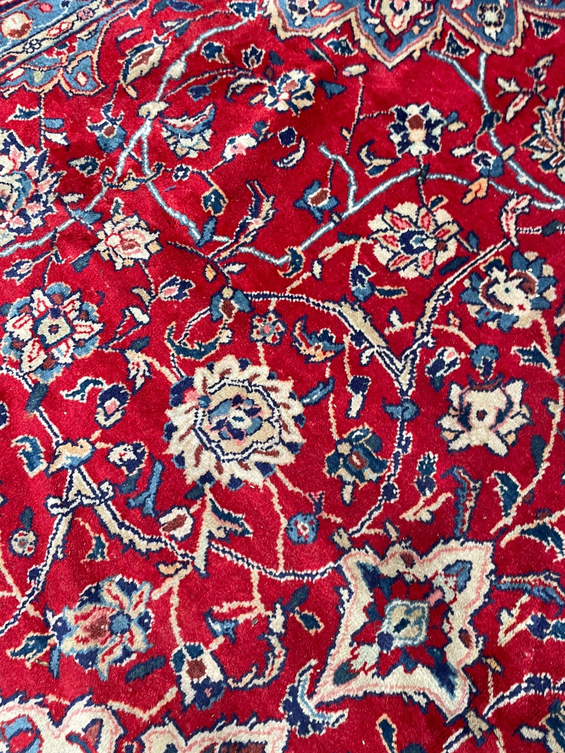 Kashan crimson ground carpet, overall floral design, the central medallion surrounded by trailing leafy branches and palmettes, scrolling border decorated with stylised plant motifs, within guard stripes