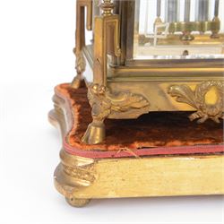 French- Art-deco Edwardian 8-day four-glass clock garniture, with etched glass panels, cast brass decoration to the corners of the case and splayed feet representing cloven hoofs to the base, case surmounted by a large oval urn on a tiered brass platform, two part dial with a recessed brass centre comprising of pierced radial decoration, with steel spade hands and Arabic numerals to the chapter, rack striking movement with a deadbeat Brocot escapement, striking the hours and half-hours on a bell. With a visible twin file mercury pendulum. Garni comprising two large twin handled urns on rectangular pedestals raised on conforming feet representing cloven hoofs, Clock and garni presented on three shaped wooden gesso bases with velvet pads. With key.