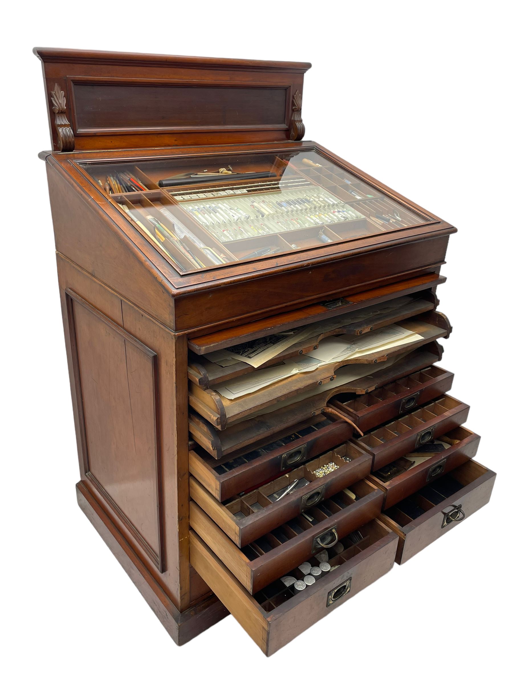 Edwardian mahogany artist's cabinet once belonging to the British artist Eli Marsden Wilson (1877-1965), raised panelled back mounted by carved brackets, sloped and hinged glazed lid enclosing paint holders and compartments, up-and-over panelled door revealing three slides, fitted with two banks of five graduating drawers with recessed brass handles, on skirted base.

Together with a quantity of artists' equipment and tools including paints, paintbrushes, charcoal, chalks, etc. and various prints relating to the life of the artist, including Quaker anti-war posters, Victorian Stevengraphs, and various chromolithographs 

Provenance: Removed from the studio of Eli Marsden Wilson. The cabinet comes to us for sale through family descent. The vendor is descendant of Marsden. Many further etchings removed from the cabinet are being sold in the Spring Art Sale, Friday 15th March 2024, Lots 265-271.

Notes: born in Ossett, Eli Marsden Wilson was the only son of Alfred Wilson, a foreman beamer, and Emma Marsden, and had five sisters. After studying at Wakefield College of Art, he moved to the Royal College of Art in London, where he became a pupil of Sir Frank Short. He had his first exhibit at the Royal Academy in 1905, the same year he married fellow artist Hilda Mary Pemberton.

A Quaker, vegetarian, and pacifist, he was a conscientious objector in World War I and as such was imprisoned in 1917 for two years. In September 1922 he was commissioned by Princess Marie Louise to produce miniature etchings for Queen Mary's Dolls' House at Windsor Castle; two such etchings are being sold in the Spring Art Sale, Friday 15th March 2024, Lot 265.