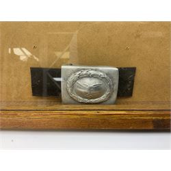 Display of eleven German belt buckles including 'SS', Party Buckle, two Army, Fire Service, two Luftwaffe, NSKK, Hitler Youth and WW1 Army; framed with three cloth badges and an armband