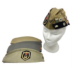 Four side caps - WW2 Russian, post-WW2 Russian and two East German; all with badges, one with multiple metal badges (4)