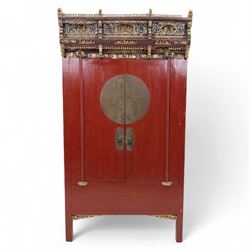 Early 20th century Chinese lacquered marriage cabinet, of rectangular form in red lacquer, fitted with double doors centred by circular brass lock plate and drop handles, the interior with shelves and two short drawers, cornice and apron with giltwood foliate and figural carving, together with an elaborately pierced and gilded wooden cresting panel carved with scenes of figures within pavilions and stylised dragons