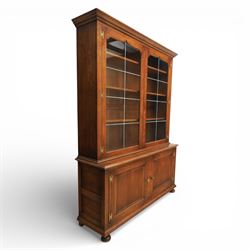 Late 20th century oak bookcase on cupboard, with moulded cornice above pair of astragal glazed doors with shaped inner frames enclosing adjustable shelves, the base with moulded top above two fielded panel cupboard doors with brass handles, upon compressed bun front feet 