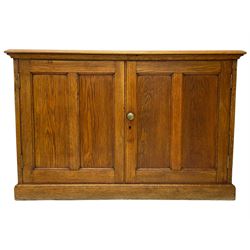 Early 20th century light oak low two door cupboard, enclosing single shelf, on skirted base