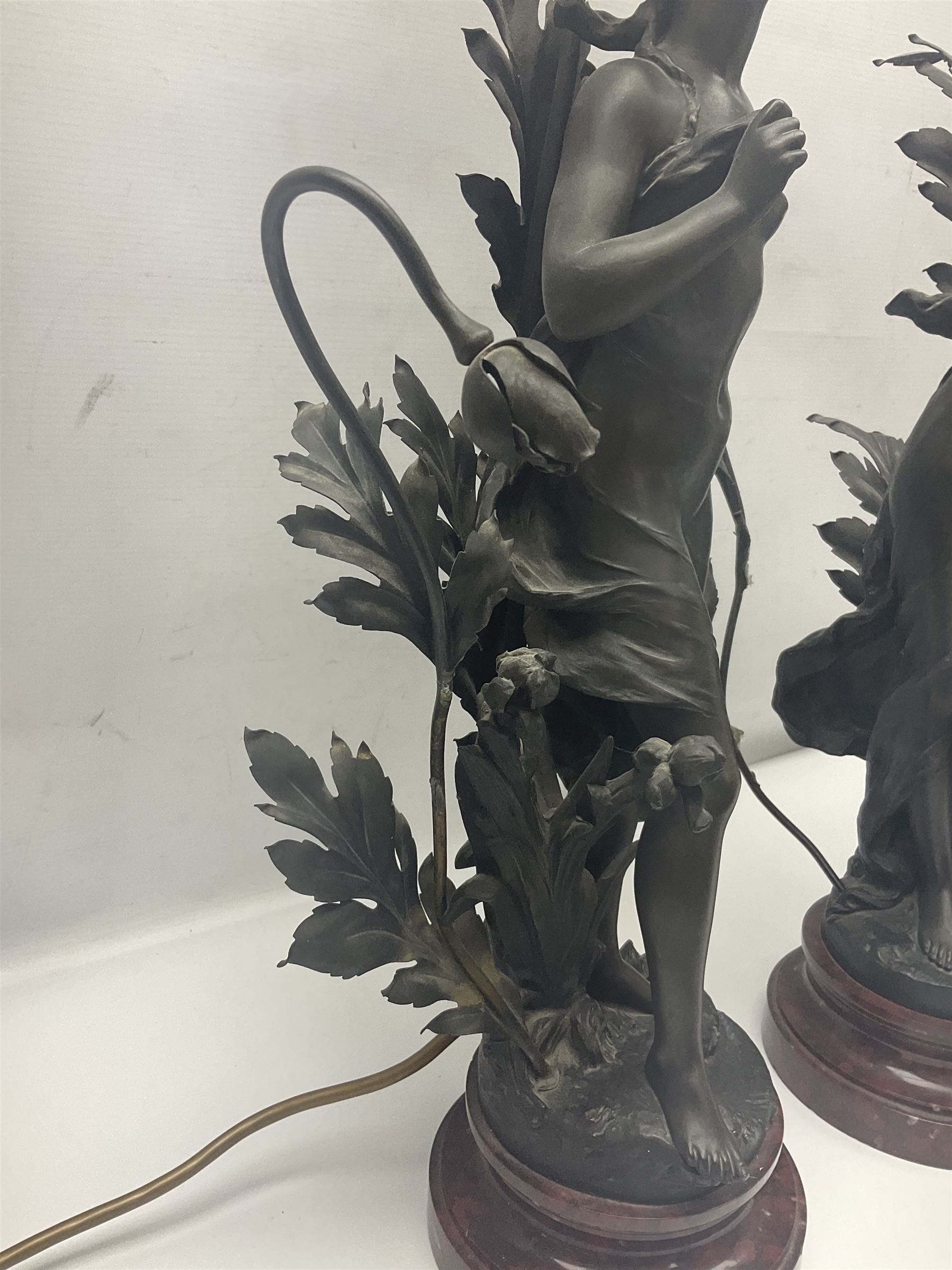 Pair of Art Nouveau style spelter figural table lamps, each mounted on rouge marble effect circular bases, with toleware flower heads and leafy decoration surrounding a female figure, H90cm