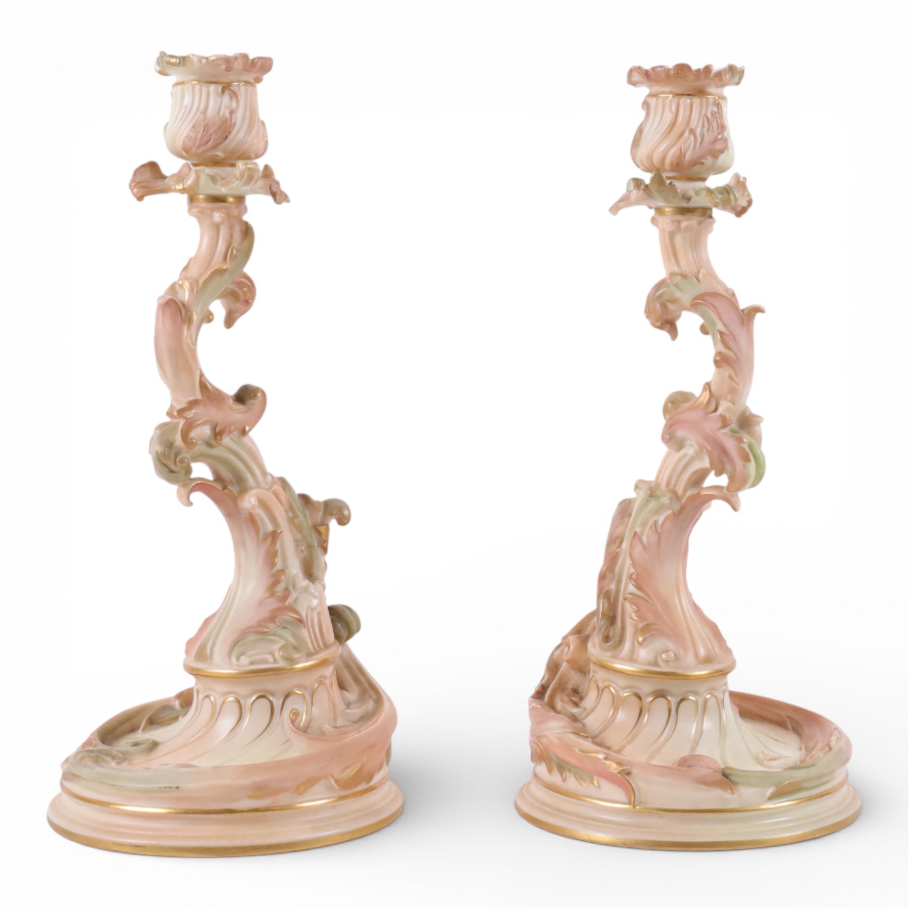 Royal Worcester pair of blush ivory candlesticks, modelled in the rococo style of scrolling foliate design upon a circular spreading base, gilt-heightened, puce mark to base and numbered RN160134 and 1478, H32cm