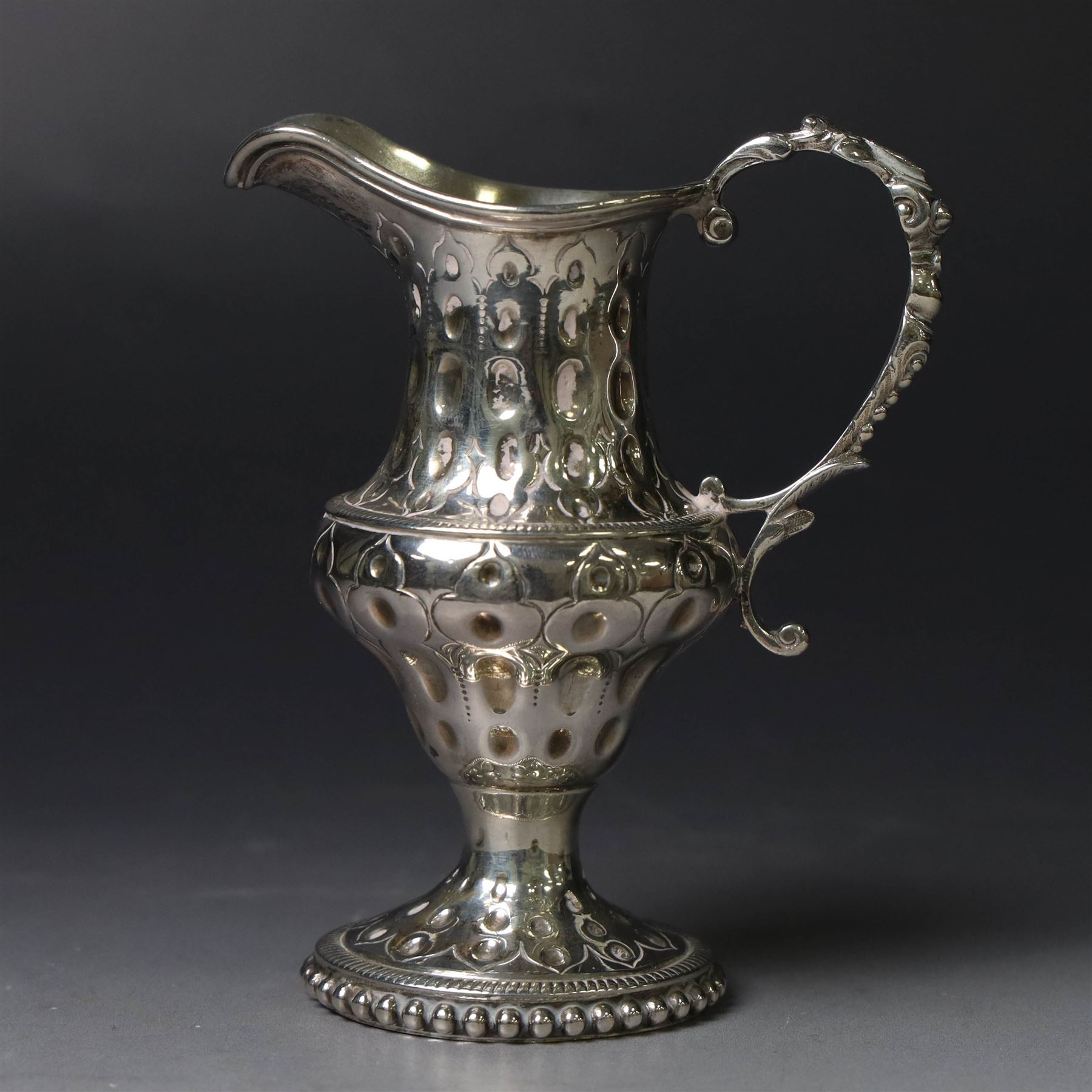 George III silver cream jug, of baluster form with hammered dimpling throughout and scroll handle, upon circular spreading foot with beaded edge, hallmarked Thomas Shepherd, London 1784, H10cm