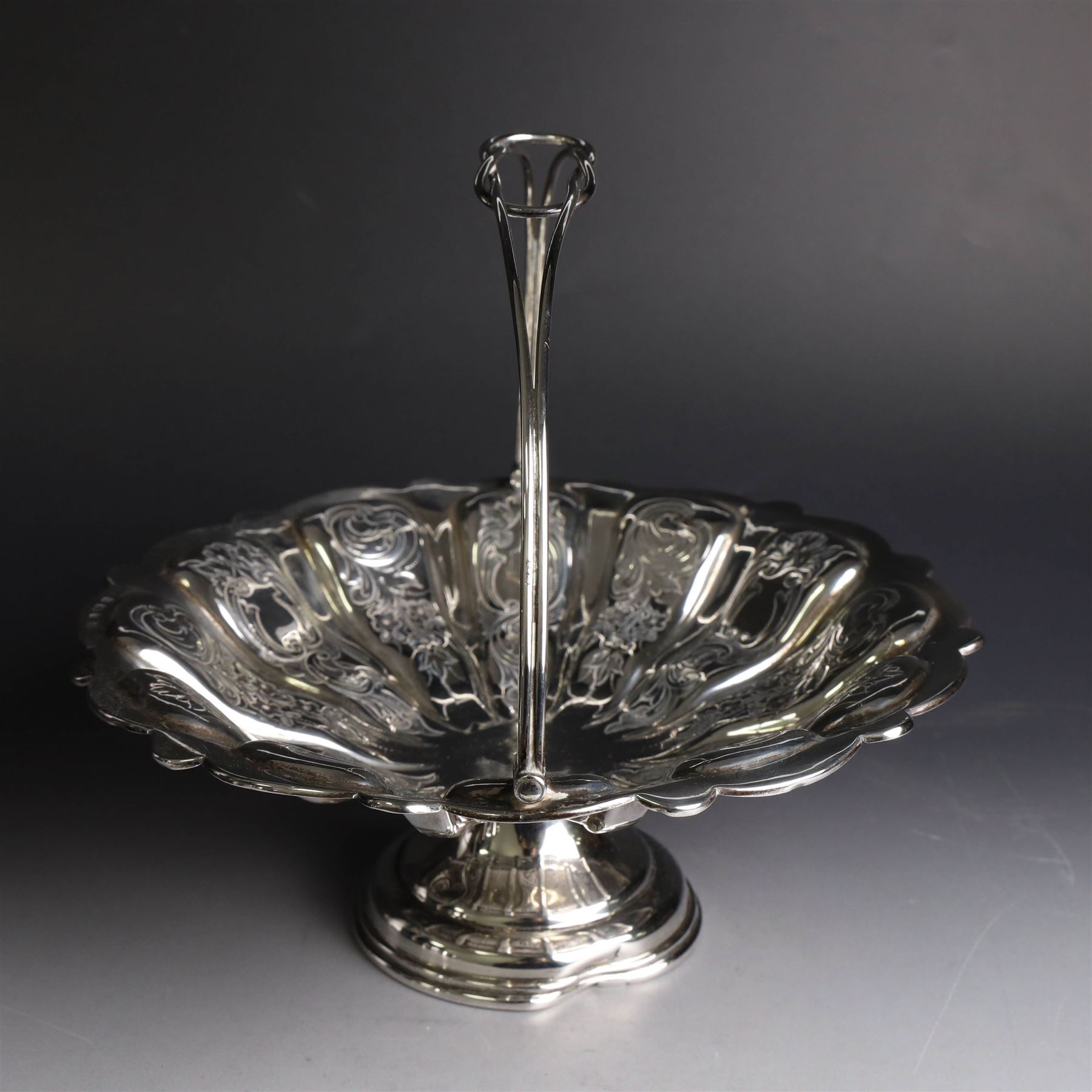 Edwardian silver swing handled basket, of circular form with shaped rim and engraved floral and foliate decoration, with know design swing handle and upon circular stepped pedestal, hallmarked J Sherwood & Sons, Birmingham 1901, H9cm, D22cm