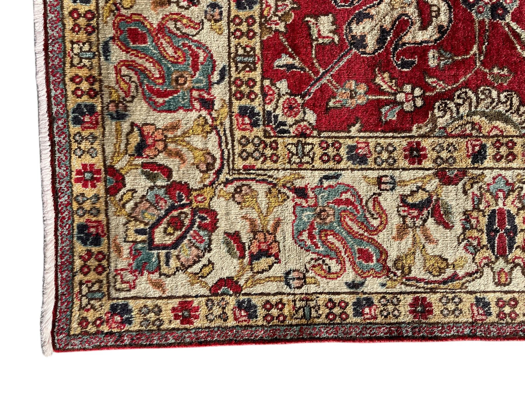 Persian Tabriz crimson ground rug, the field decorated with large palmette and stylised plant motifs connected by interlaced leafy branches, trailing border decorated with similar palmette motifs within floral pattern guard stripes, with signature panel 
